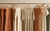 Una hilera de vestidos de diseño colgados armónicamente en un perchero de madera clara dentro de una boutique iluminada.