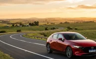 Un Mazda 3 de última generación transitando con fluidez por una sinuosa carretera de colinas durante el atardecer.
