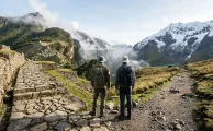 Dos senderistas en un camino de piedra andino con un nevado al fondo, imagen que ilustra la comparación Camino Inca vs Salkantay